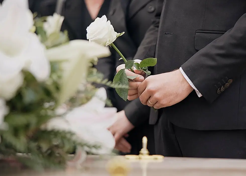 Ein Mann hält eine weiße Rose bei einer Beerdigung in der Hand